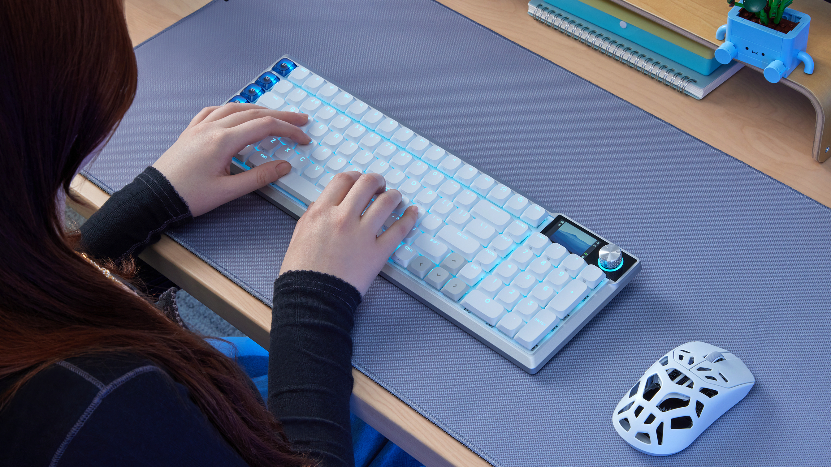 Person typing on a white VANGUARD AIR 99 wireless keyboard with blue LED backlighting at a wooden desk.