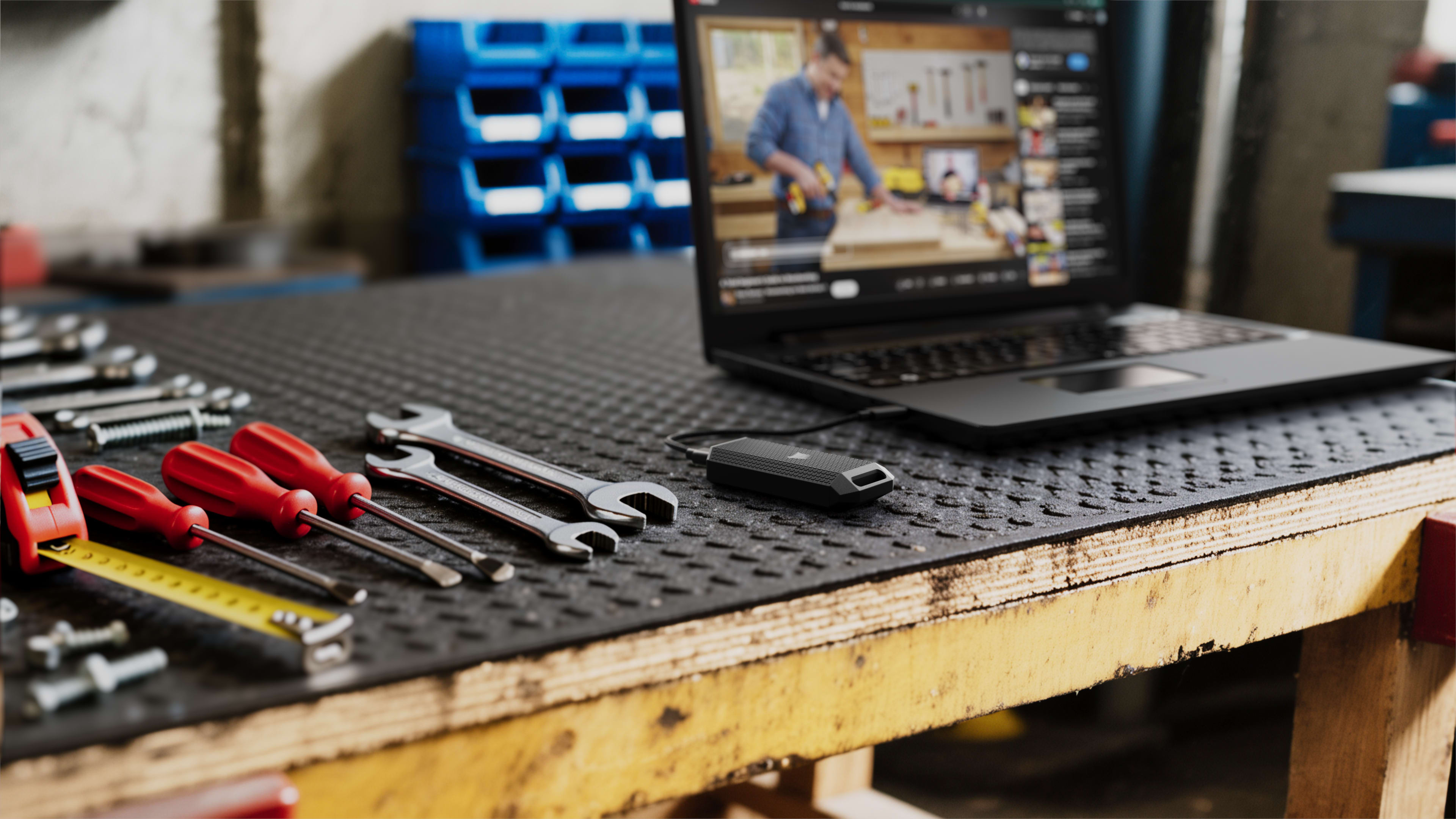 CORSAIR EX400U Survivor portable SSD on a workshop bench with hand tools and a laptop in the background.