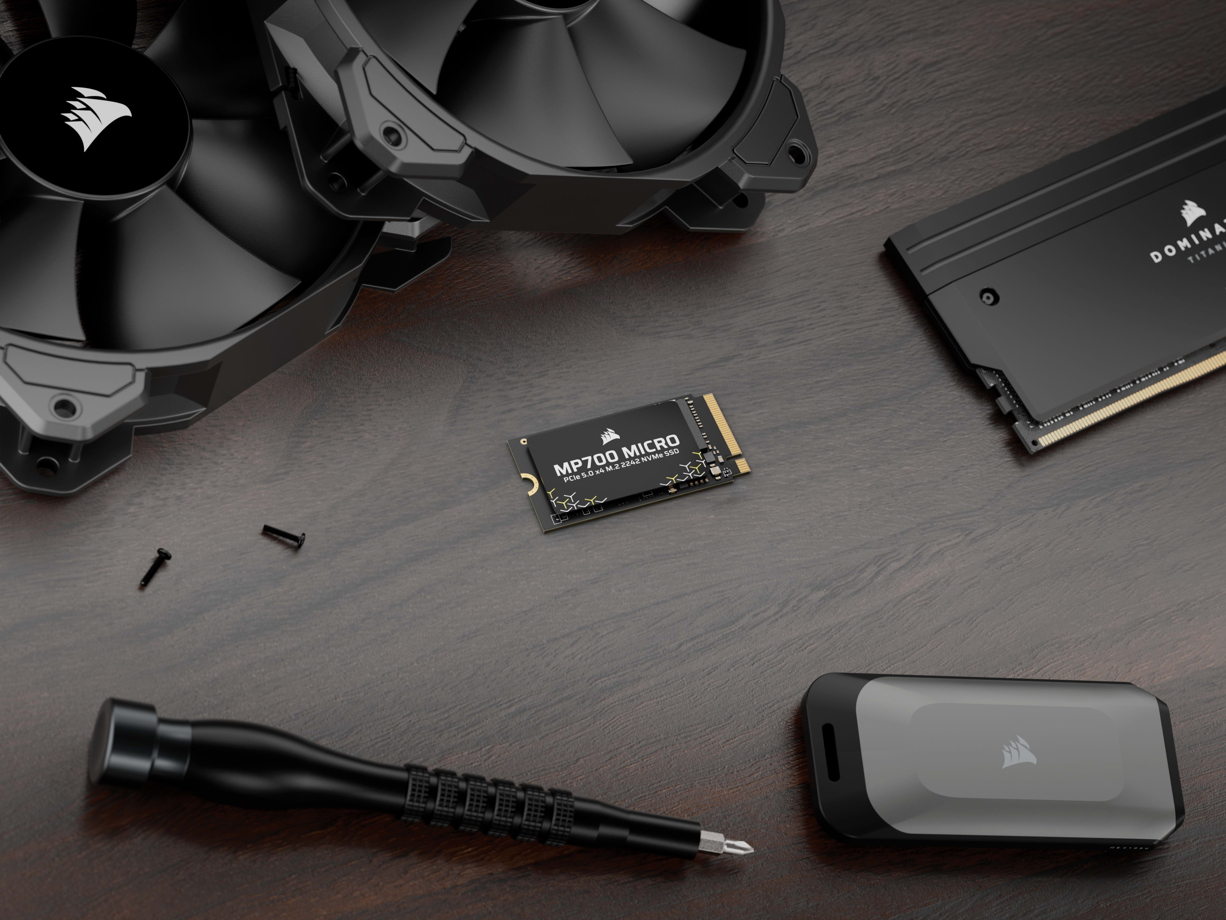 CORSAIR MP700 MICRO SSD displayed alongside a case fan, DOMINATOR RAM, and screwdriver on a dark wooden surface.