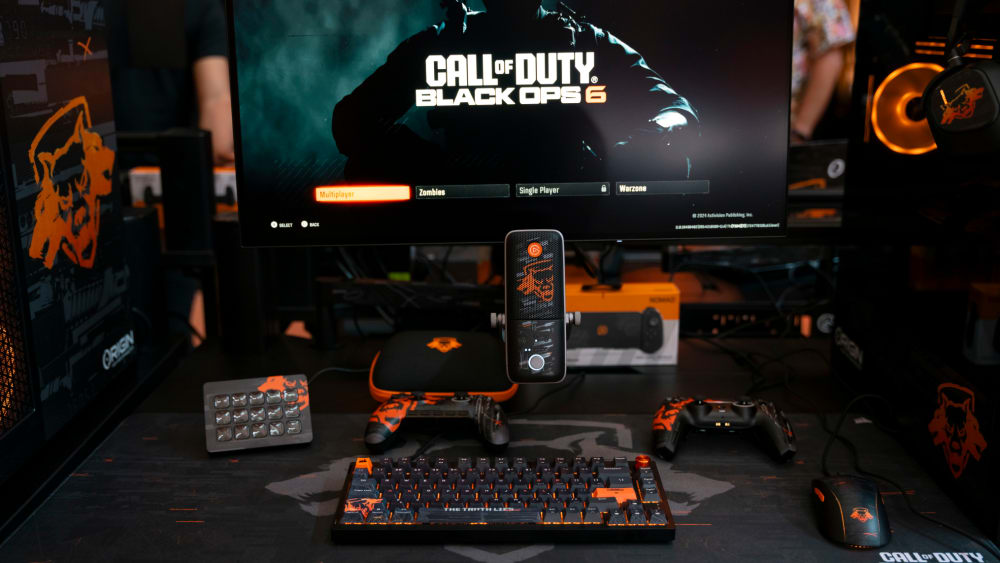 A complete Call of Duty® Black Ops 6 desk setup, with a CORSAIR K65 WIRELESS 75% RGB Mechanical Gaming Keyboard, Elgato Stream Deck, Elgato Wave:3 Microphone, and SCUF Reflex FPS (PS5) and Reflex Pro Gaming Controllers (with case) on the CORSAIR MM300 Gaming Mouse Mat—all in Call of Duty® Black Ops 6 Editions.